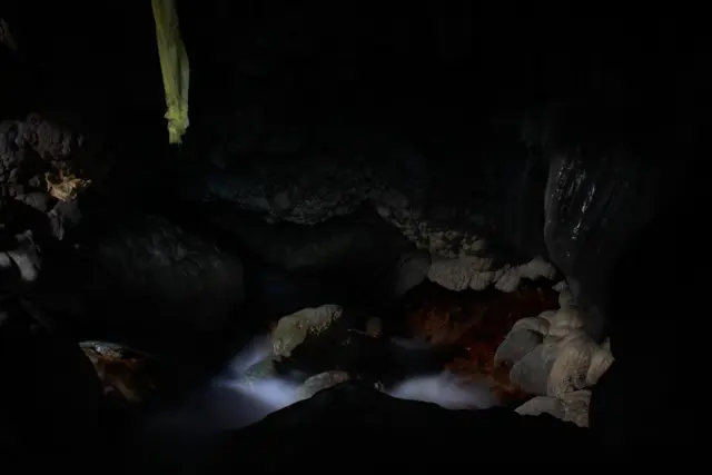 Water flowing between pale rock formations in a dark cave