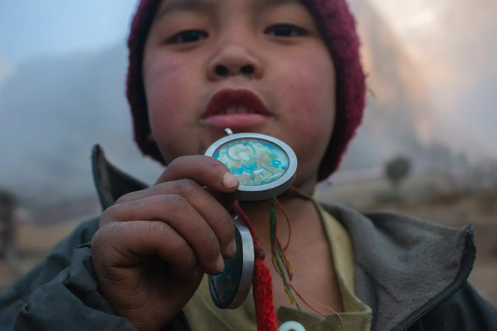 Child in a red woolly hat holding up a Guru Rinpoche amulet
