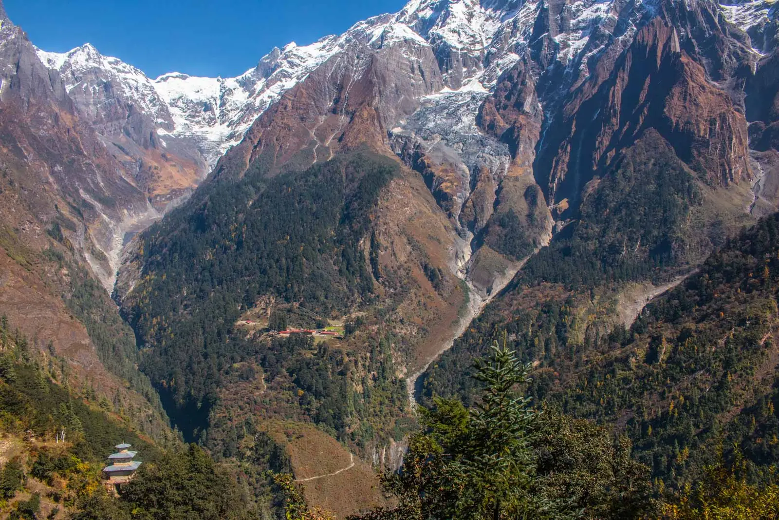 Deep forested valley below snowy cliffs, with a pagoda-roofed temple below