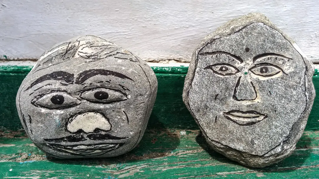 Two stones painted with simple human faces on a green ledge