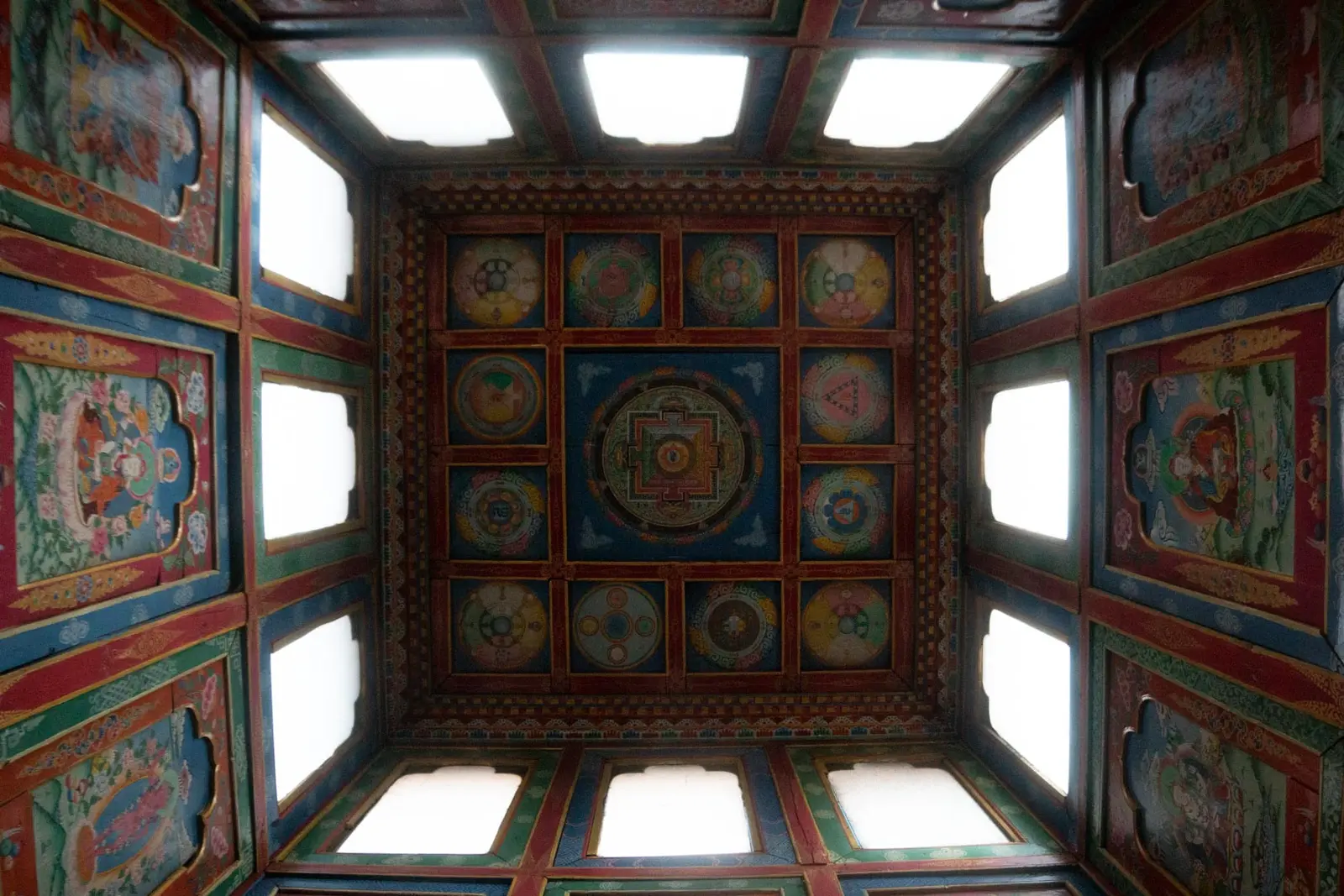 Painted mandala ceiling framed by skylights inside a monastery