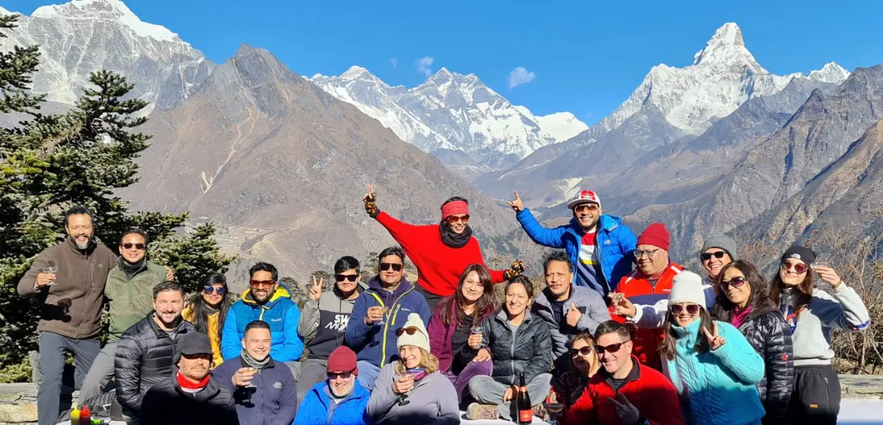 Large group with drinks on a terrace with Everest and Ama Dablam mountains behind