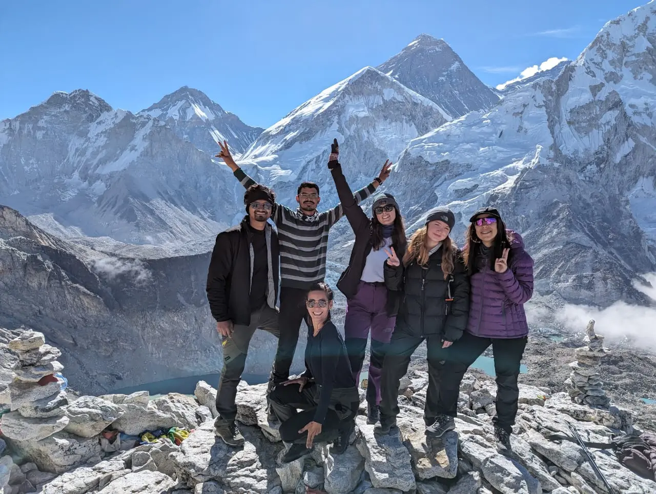 Six trekkers posing on summit rocks with Everest mountain behind