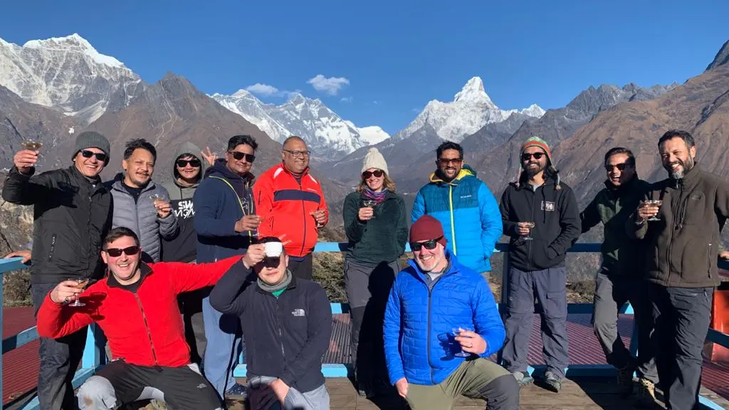 Group raising glasses on a hotel terrace with Ama Dablam and Everest mountains behind