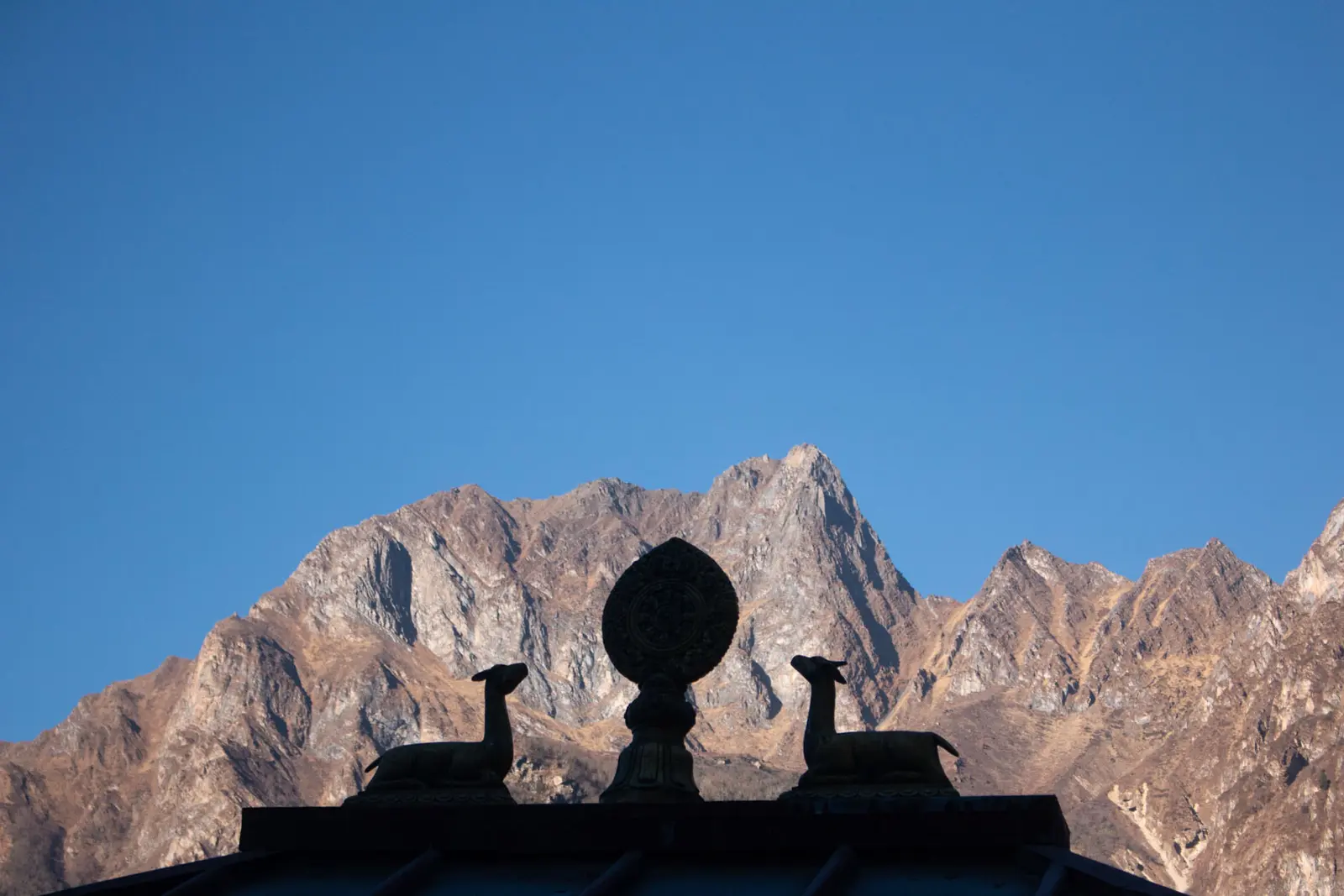 Silhouette of a dharma wheel and deer rooftop ornament against rocky mountains