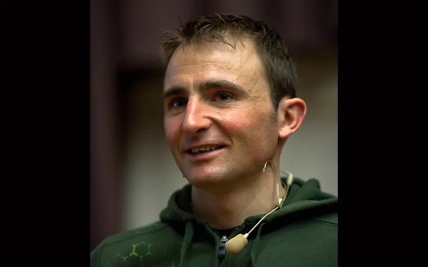 Smiling man with short hair wearing a headset microphone and green hoodie