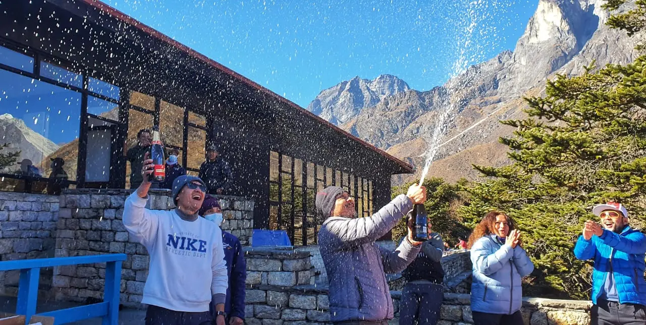 Group spraying champagne outside a stone hotel with mountains behind