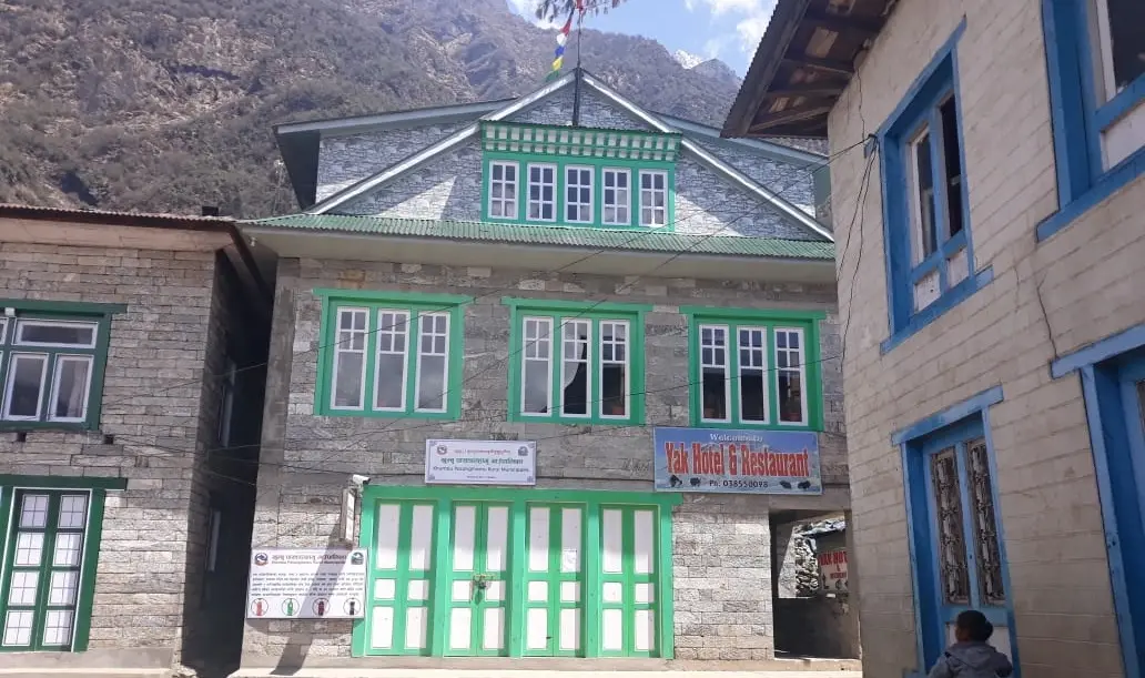 Stone building with green windows and signboards on a lane in Lukla