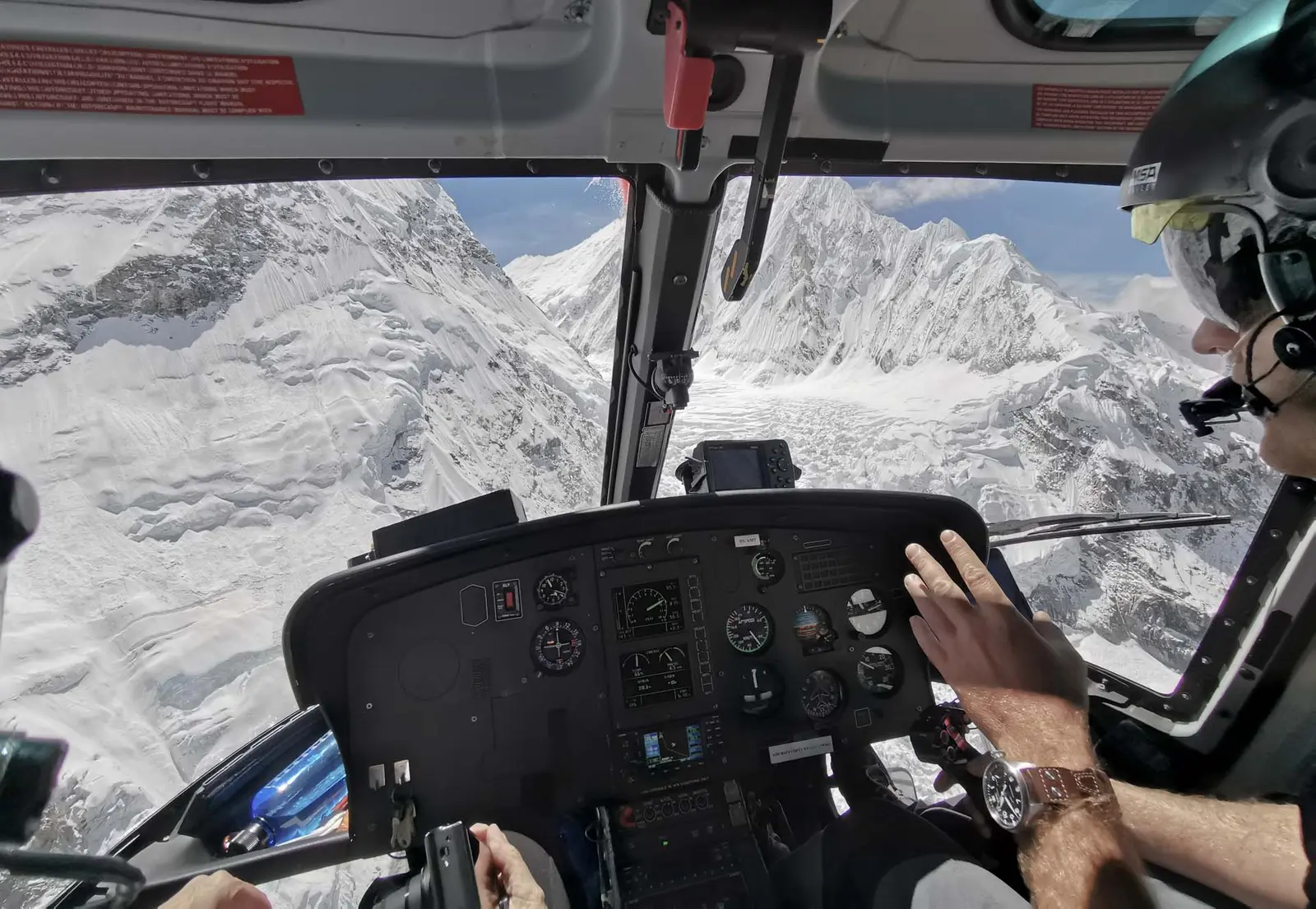 Pilot's view from a helicopter cockpit over a glacier and snowy peaks